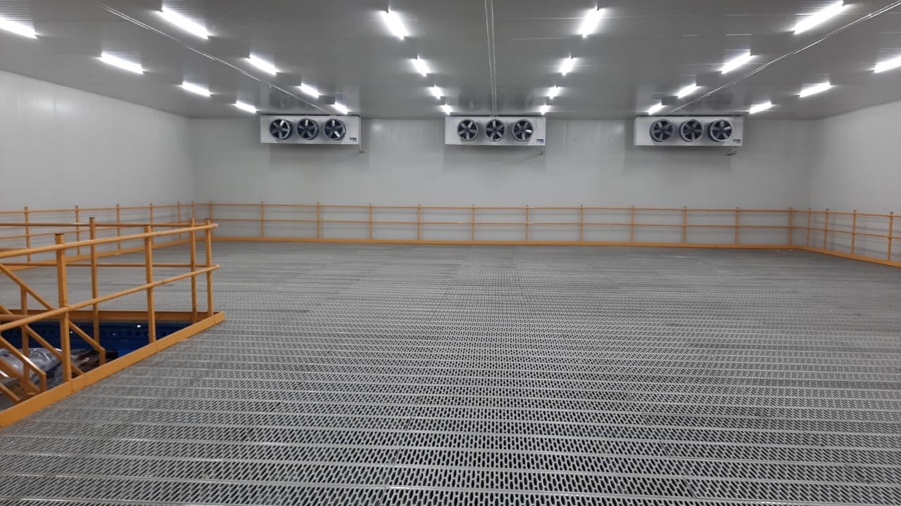 Cold storage interior — evaporator fan units, perforated floor, and orange safety railings